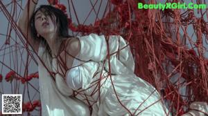 A woman in a white dress is tied up to a rope.