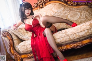 A woman in a red dress sitting on a couch holding a glass of wine.