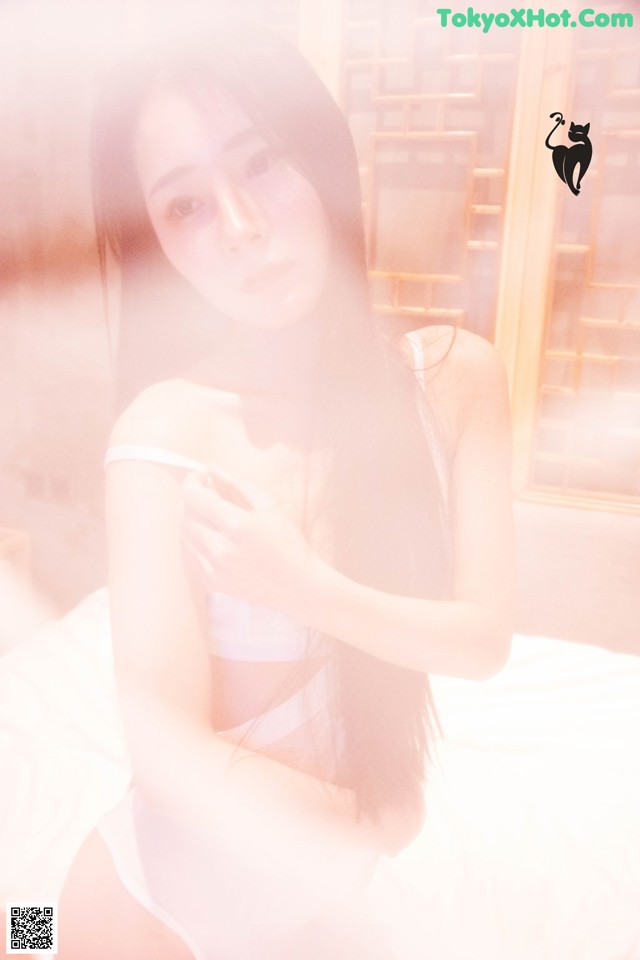 A woman in a white lingerie sitting on a bed.