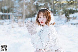 A woman in a white dress and red hat sitting in the snow.