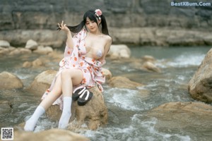 A woman in a bikini standing on a rock by the water.