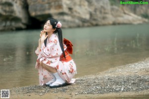 A woman in a bikini sitting on a rock by the water.