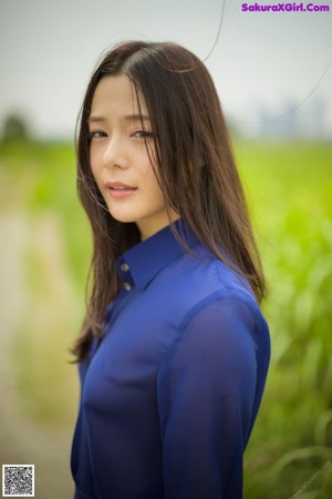 A woman in a blue shirt is posing in the woods.