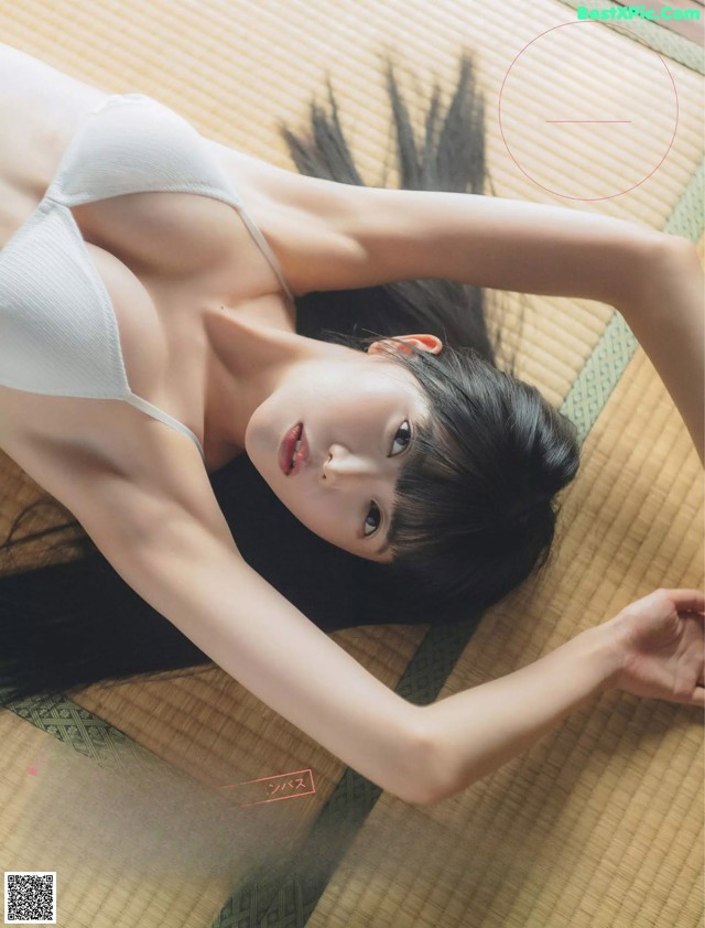 A woman in a white bra laying on a bamboo mat.