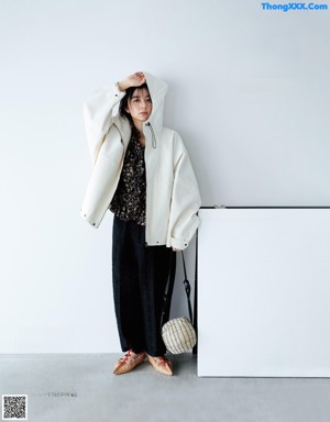 A woman wearing glasses standing in front of a white wall.