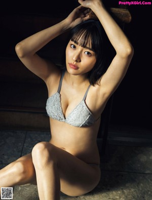 A woman in a white bra sitting on a blue pillow.