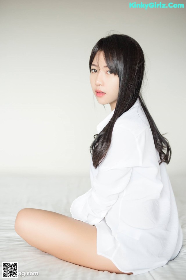 A woman sitting on a bed wearing a white shirt.