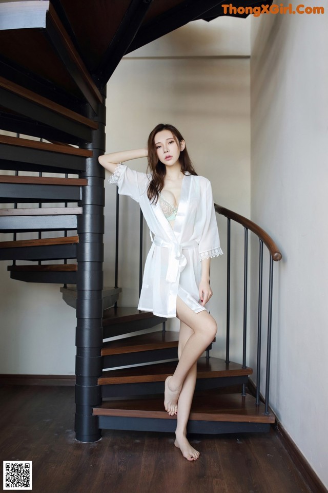 A woman in a white robe standing on a wooden staircase.