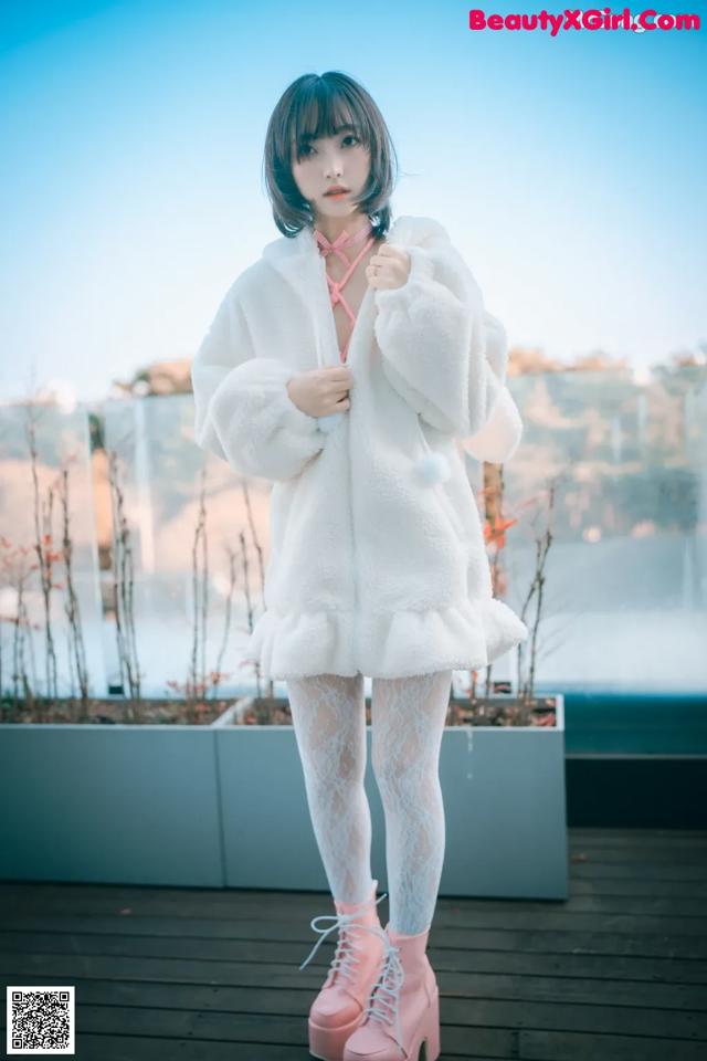 A woman in a white coat and pink boots posing for a picture.