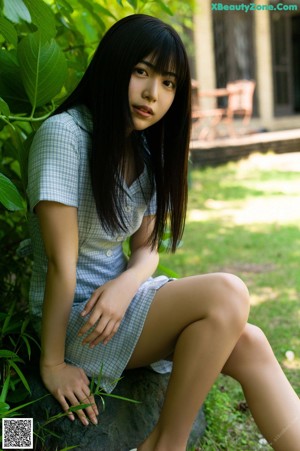 A young woman with long black hair sitting in the grass.