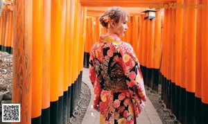 A woman in a green and blue dress standing in front of a bamboo fence.