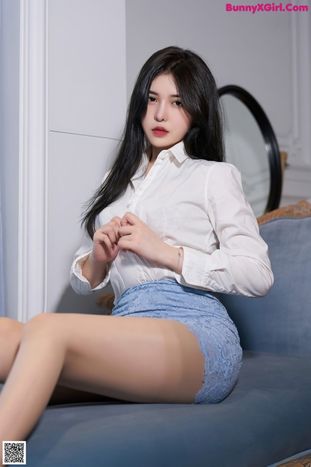 A woman sitting on a blue couch wearing a white shirt and blue skirt.