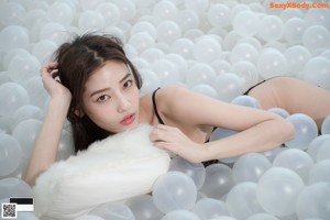 A woman laying on top of a bed of white balloons.