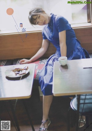 A woman in a blue dress sitting at a table with a cup of coffee.