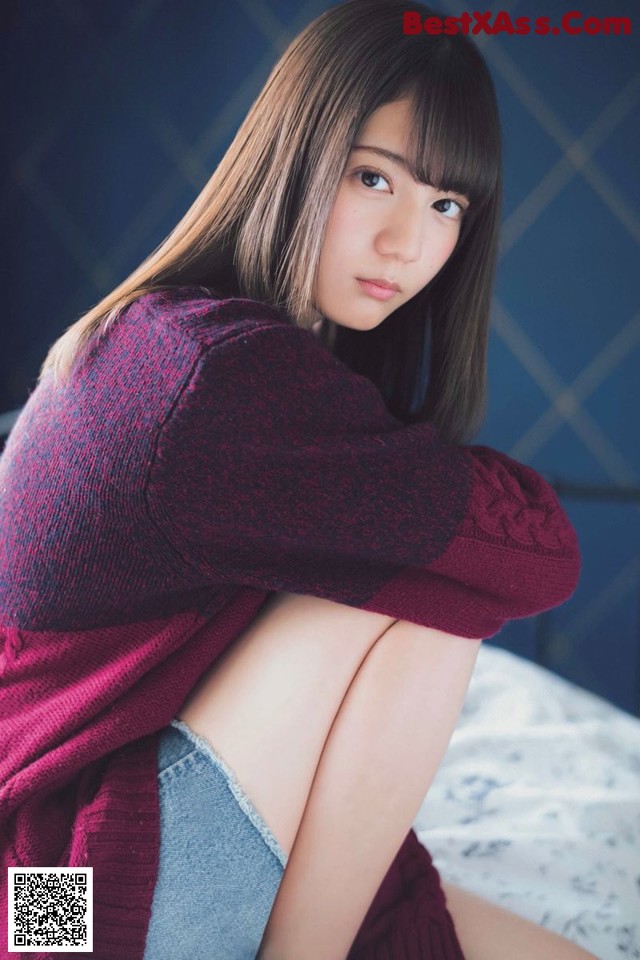 A woman sitting on top of a bed wearing a red sweater.