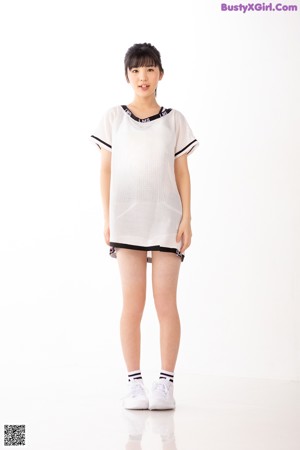 A woman in a white shirt and black shorts leaning against a wall.
