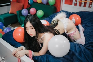 A woman in lingerie sitting on a bed with balloons.