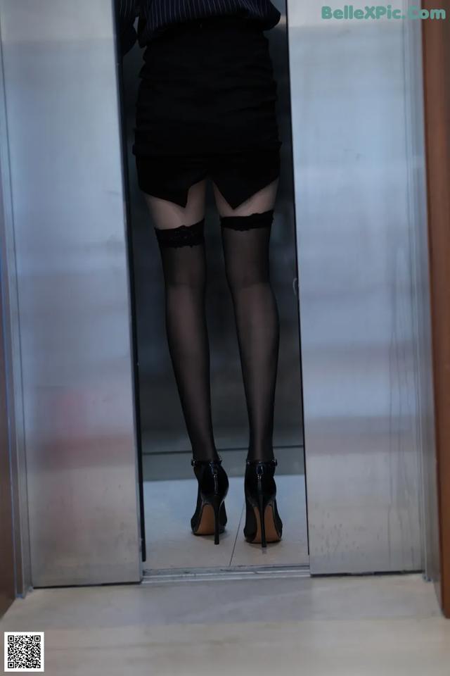 A woman in black stockings and high heels standing in an elevator.