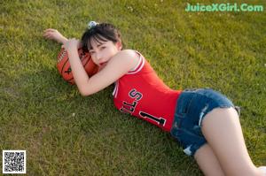 A woman in a red shirt and blue shorts holding a basketball.